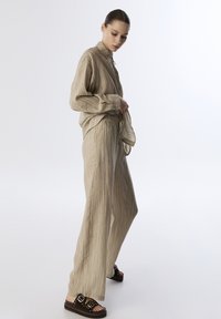 Conjunto de dos piezas en color beige que incluye una camisa de botones con rayas verticales y pantalones anchos relajados con cintura elástica.