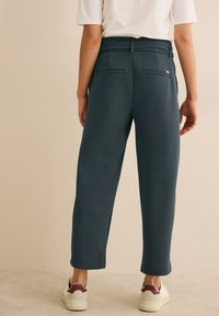 Pantalons relaxed-fit bleu foncé, avec un taille élastique et deux poches au dos. Texture lisse et fuselés aux chevilles. Associés à des baskets blanches.