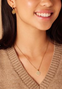 Gouden sieradenset met een hangerketting en oorbellen met hoepels, beiden met boomontwerpen. De ketting heeft een fijne schakel en een ronde hanger.