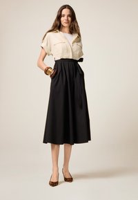 Blusa beige a maniche corte con due tasche abbinata a una gonna midi nera fluida con vita legata. Indossata con décolleté con stampa leopardata.