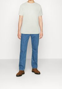 Svetle šedé tričko s kulatým výstřihem, modré džíny rovného střihu a hnědé kotníkové boty. Oblečení má jednoduchý, ležérní design.