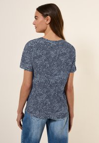 T-shirt bleu marine avec un motif ondulé blanc, à manches courtes et encolure ronde, associé à un jean en denim bleu clair.