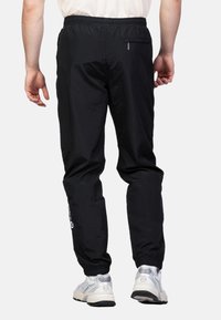 Zwarte lichtgewicht joggingbroek met een elastische tailleband en boorden, voorzien van een ritsachterzak en logo-detail op het linkerbovenbeen.