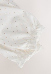 White fabric with small beige polka dots and elasticated cuffs, likely part of a garment sleeve or pant leg.