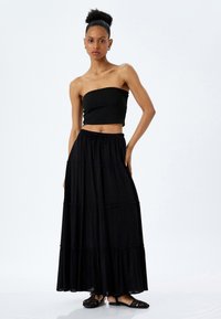 Top negro sin tirantes y larga falda negra de capas hecha de tela ligera, con cintura elástica y textura sutil.