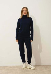 Granatowy dzianinowy golf i pasujące spodnie z miękkiego materiału. Białe sneakersy dopełniają stylizację. Prosty, dopasowany krój z prążkowanymi mankietami.