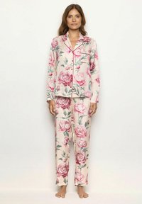 Set de pijama din material moale cu un imprimeu mare de bujori roz pe un fundal bej, incluzând o cămașă cu nasturi și pantaloni asortați.
