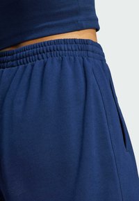 Mörkblå träningsoverallsbyxor med elastisk midja, sidfickor och ett mjukt, texturerat tyg. Designade för komfort och rörelsefrihet.