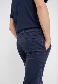 Laivaston siniset samettivahverohousut, joissa näkyvät pystysuorat uurteet, istuva malli ja sivutaskut. Yksinkertainen vyötärönauha ilman näkyviä metalliosia.