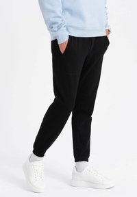 Zwarte joggingsbroek gemaakt van zachte stof, met elastische boorden en zijzakken, gecombineerd met witte sneakers en een lichtblauwe sweatshirt.