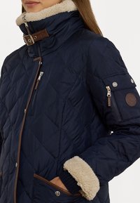 Mornarska jakna s prešivanjem i visokim ovratnikom, u kombinaciji s smešnim kožnim detaljima i flis podstavom. Sadrži zip džep i udoban detalj na manžetama.