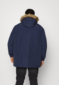 Mörkblå parka-jacka med huva med konstpäls, elastiska ärmar och en medellång skärning, med en slät yta och minimalistisk design.