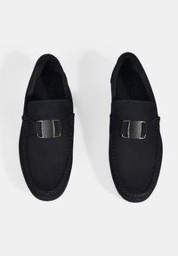 Schwarze Wildleder-Lederhausschuhe mit einem silbernen Schnallenakzent. Verfügt über blaue Stickerei entlang der Kante und eine glatte, strukturierte Außenseite. Flaches Design.