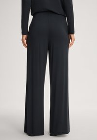 Schwarze, weit geschnittene Hose aus einem glatten, dehnbaren Stoff. Mit einem elastischen Bund und einem lockeren Schnitt, der bis zum Boden reicht.