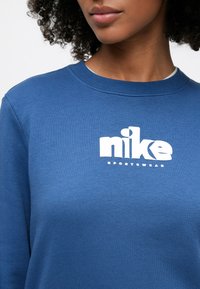 Μπλε φούτερ από απαλό ύφασμα με λευκό λογότυπο Nike στο στήθος και στρογγυλή λαιμόκοψη. Κλασική γρ αμμή με ριμπ λεπτομέρειες.