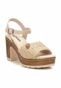 Sandalia de plataforma beige con empeine trenzado, correa ajustable en el tobillo y un tacón alto marrón. Presenta un logo decorativo en la correa.