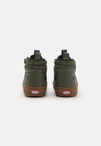 Zelené vysoké tenisky s černými detaily, vybavené polstrovaným límcem, texturovaným povrchem a hnědými gumovými podešvemi. Červené logo je viditelné na patě.