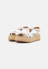 White sandal with crossed straps and ankle buckle. Features woven beige platform sole and cushioned insole for comfort. Subtle logo detail.