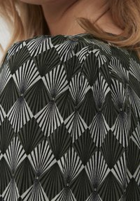 Grön och svart mönstrad tyg med en geometrisk design av växelvis diamanter med linjära accenter. Texturerad yta synlig.