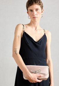 Sac à main en cuir rose doux, avec un accent en nœud argenté et des coutures contrastantes. Le sac est rectangulaire avec une texture lisse.