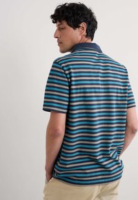 Tricou polo cu mânecă scurtă, cu dungi orizontale în nuanțe de albastru, albastru deschis, gri și albastru închis. Are o căptușeală clasică și o textură moale a materialului.