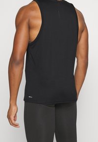 Haut de sport noir sans manches avec une finition texturée, comportant une étiquette "DRYCELL" sur le côté inférieur. Coupe ajustée et détail au dos.