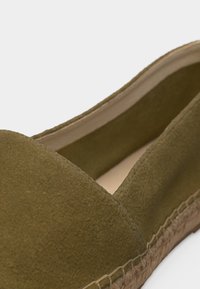Gros plan d'une espadrille en daim vert olive avec semelle en jute tressée et doublure intérieure beige.