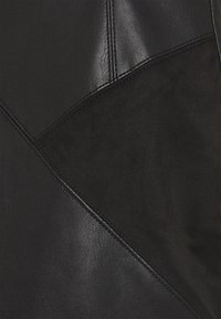 Chaqueta de cuero negra que presenta una combinación de texturas lisas y de ante, con un diseño de patchwork angular y detalles de costura visibles.