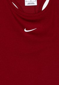 Rdeča ribičasta majica na naramnice z okroglo izrezom in belim Nike logotipom na prsih. Tkanina se zdi gladka in raztegljiva, primerna za aktivno nošenje.