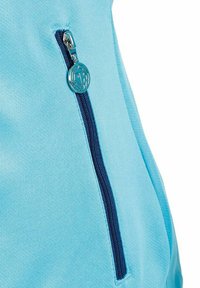 Lichtblauw stof met een verticale donkerblauwe rits, voorzien van een ronde metalen trekker met een geometrisch logo erin gedrukt.