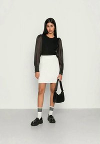 Blusa preta de manga longa com mangas transparentes, saia mini texturizada branca, mala preta de ombro, meias listradas e sapatos plataforma pretos.