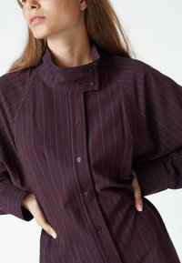 Dark purple button-up shirt with vertical blue stripes, high collar, and tailored fit. Features subtle sewing details and standard button closure.