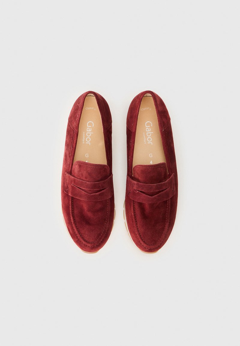 Rode suède instappers met een gestikt ontwerp, voorzien van een decoratieve band over de volzijde en een beige rubberen zool.