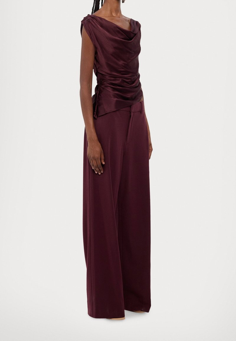 Haut en satin drapé bourgogne avec des manches courtes, associé à un pantalon taille haute, ample, présentant une texture lisse et des lignes épurées.