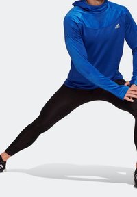 Felpa atletica a maniche lunghe blu con colletto alto e aperture per i pollici, abbinata a leggings neri aderenti. Tessuto morbido, branding minimale.