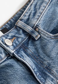 Sinine teksade vöökoht lähedalt, nähtav nupp, vööaas ja oranžid õmblused.