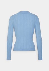 Pull en maille côtelée bleu clair au design ajusté, à manches longues et col structuré. Le tissu texturé renforce les détails visuels.