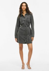 Traper haljina u izbljeđenoj crnoj boji s dugim rukavima, dugmadi sprijeda, džepovima na prsima i remenom u struku za prilagođeni izgled.