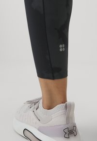 Leggings atléticos pretos com um padrão escuro subtil, combinados com ténis cinzentos claros com um design texturizado e uma sola branca.
