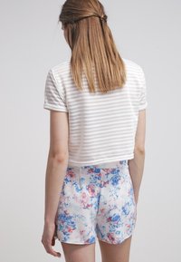 Chemise blanche rayée, courte, à manches courtes, associée à un short imprimé floral aux tons bleus et roses, avec un tissu texturé.