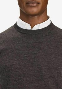 Grå tröja i stickad tyg, med rund halsringning, bärs över en vit skjorta med krage. Slät struktur med ett enkelt mönster.