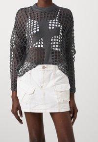 Suéter gris de punto abierto con mangas largas, que presenta un diseño de cruz central, combinado con una falda mini blanca con bolsillos de carga.