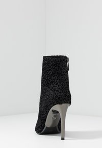 Stivale alla caviglia nero con motivo leopardato, texture in camoscio, punta affusolata e tacco a stiletto sottile. Presenta una cerniera sul lato.