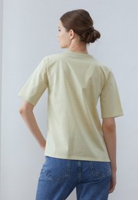 Tricou din bumbac de culoare galben deschis, cu mâneci scurte, decolteu rotund și o croială lejeră, asortat cu blugi din denim albastru. Fără modele sau accente vizibile.