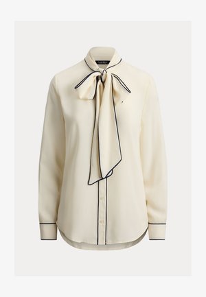 Εκρού μπλούζα με γιακά που δένει σε φιόγκο, σκούρα μπλε περίγραμμα, μακριά μανίκια, κούμπωμα με κουμπιά και απαλό ύφασμα. Κομμένη και ραμμένη εφαρμοστή, με κυρτή βάση.