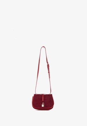 Rode suede handtas met een gebogen vorm, voorzien van een ritssluiting, gouden hardware en een afneembare schouderband. Glad textuur, minimale accenten.