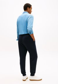 Světlomodrá džínová košile s vyhrnutými rukávy, doplněná tmavě modrými tepláky s bočními kapsami a bílými teniskami s gumovými podrážkami.