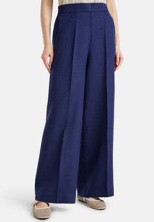 Spodnie o szerokich nogawkach w granatowym materiale. Charakteryzują się wysokim stanem, dwoma przednimi plisami i gładką fakturą. Połączone z beżowymi siateczkowymi butami wsuwanymi.