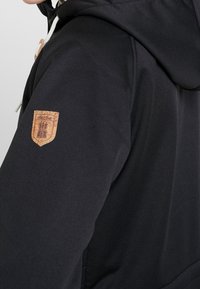 Czarna kurtka z kapturem z korkową naszywką na lewym rękawie, z troczkami i gładkim, teksturowanym materiałem.