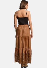 Jupe maxi marron avec un design à volants, ornée de dentelle brodée au bas, associée à un haut à fines bretelles noir.